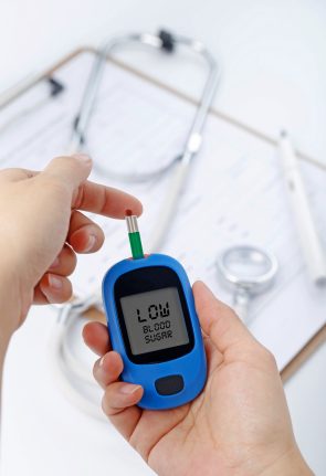 hand-holding-blood-glucose-meter-measuring-blood-sugar-background-is-stethoscope-chart-file